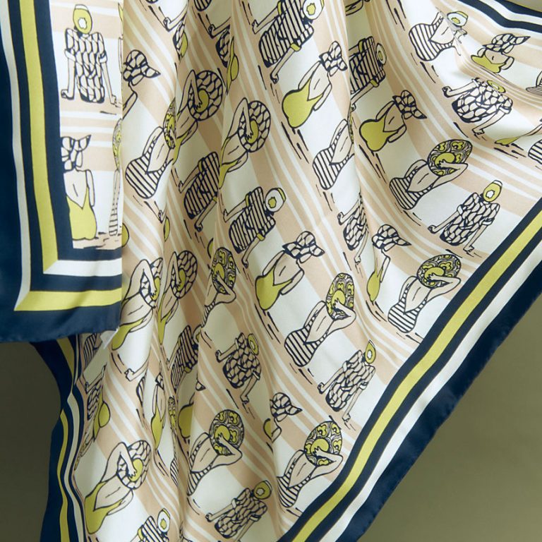 Visuel d'un foulard qui flotte dans l'espace. Sur ce carré de soie sont dessinées des petites baigneuses sur fond de rayures marines.